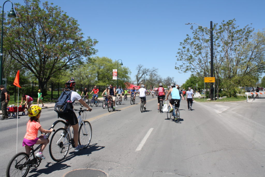A photo of a sunny day at Síclovía. The photo shows people riding their bikes down a street closed to cars.