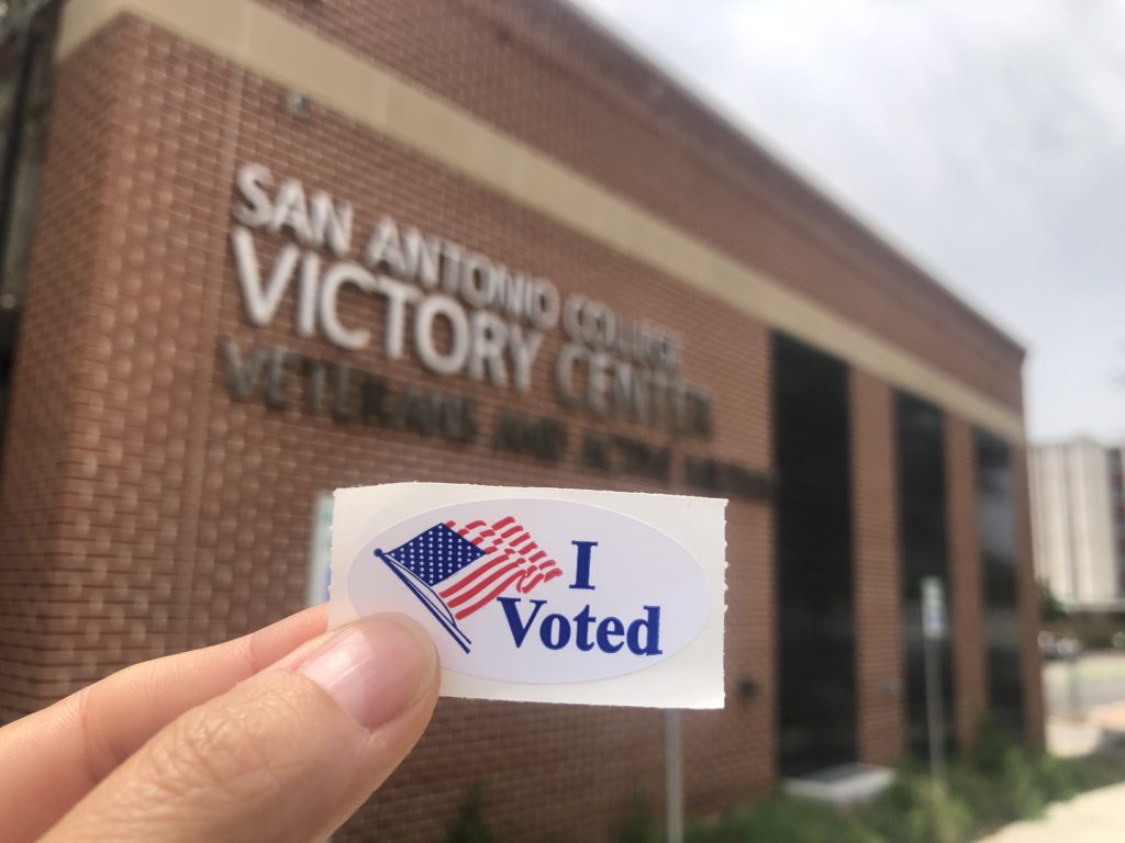 A hand holds an "I voted" sticker in front of the San Antonio College Victory center polling center