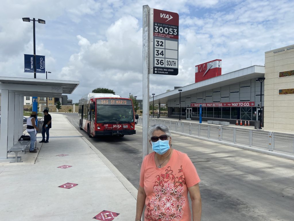 Dolores Vara stands in front of a VIA bus and bus stop sign at the Brooks Transit Center